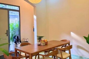 A dining area with a wooden table and chairs, a bowl of fruit, and a potted plant.
