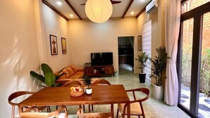 A dining area with a wooden table and chairs, a television, and a large plant. - LYLAC Home Saigon TDX - City Center Cosy 4BR Townhouse with Garden in D1 (Ho Chi Minh City)