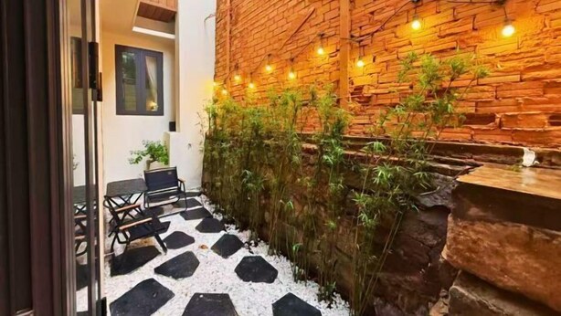 A courtyard with a brick wall, string lights, a seating area with chairs, and a small table. - LYLAC Home Saigon TDX - City Center Cosy 4BR Townhouse with Garden in D1 (Ho Chi Minh City)