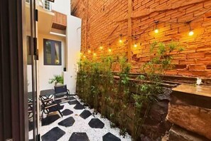 A courtyard with a brick wall, string lights, a seating area with chairs, and a small table.