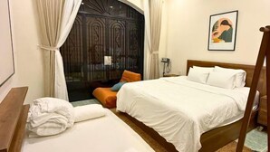 A bedroom with a bed, pillows, a bedside table, a window with curtains, and a door with a decorative design. - LYLAC Home Saigon TDX - City Center Cosy 4BR Townhouse with Garden in D1 (Ho Chi Minh City)