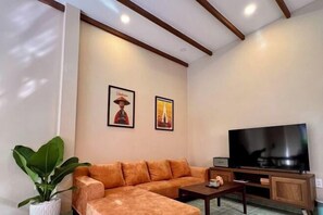 A living room with a sofa, a television, and two framed pictures on the wall.