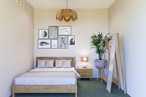 A bedroom with a bed, wall art, a hanging light fixture, a bedside table with a lamp, and a potted plant.