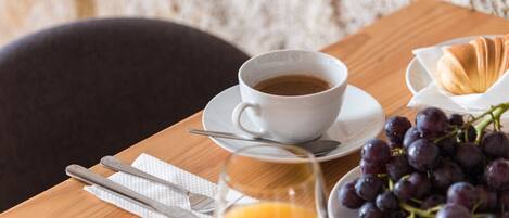 A wooden table with a white cup of coffee, a plate of grapes, a glass of orange juice, and a croissant.