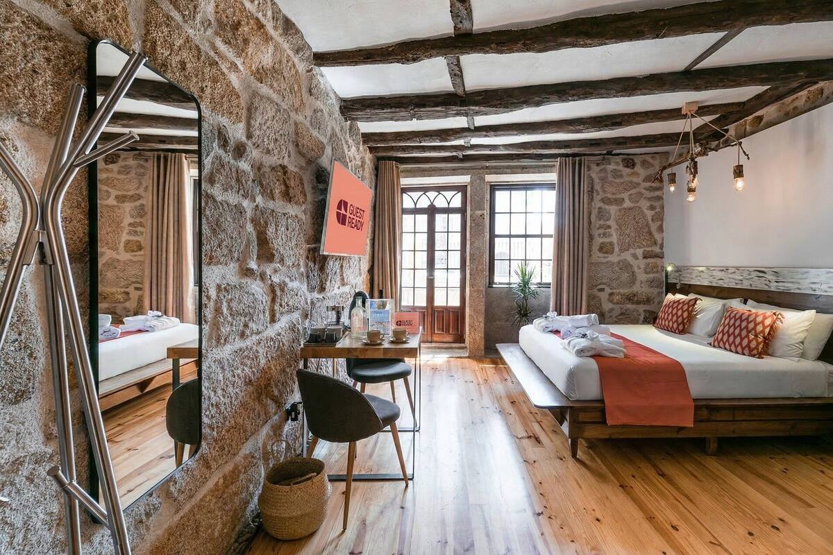 A rustic room with stone walls, a wooden bed, a desk with a chair, and a 'GUEST READY' sign.