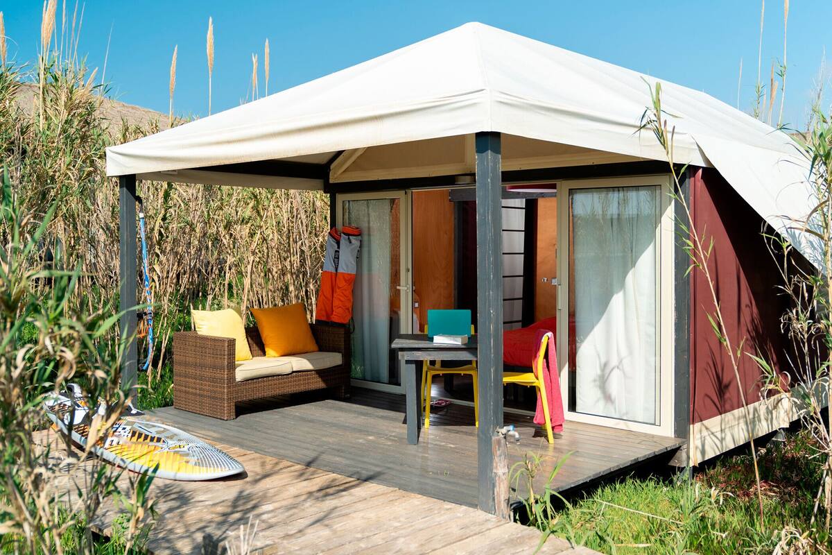 A tented accommodation with a wooden deck, a sofa with cushions, a table, and a chair.