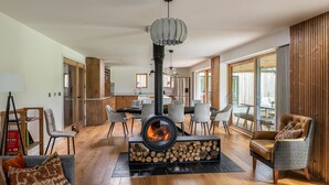 Un salon moderne doté d’un poêle à bois, d’un coin repas et d’un espace détente confortable avec un canapé et des fauteuils.