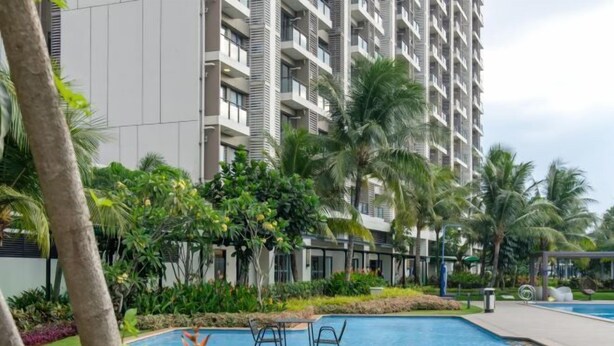 A modern hotel with a swimming pool, surrounded by lush greenery and palm trees. - Calma 2BR II @Skyhouse Apartment (Cisauk)
