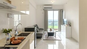 A modern kitchen with a dining area, a sofa, and a view of the outdoors. - Calma 2BR II @Skyhouse Apartment (Cisauk)