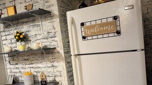 A kitchen with a white refrigerator, a 'Welcome' sign on the door, and shelves with kitchenware and decorative items. - Convenient 1-BR - Fenced Backyard - Extended Stays wanted (Huntington)