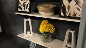 A shelf with a woven basket, a vase with yellow flowers, and framed artwork. - Convenient 1-BR - Fenced Backyard - Extended Stays wanted (Huntington)