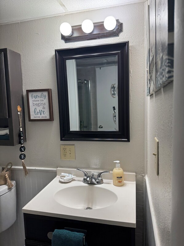 A bathroom with a white sink, a mirror with a black frame, and a 'family where life begins & love never ends' sign.