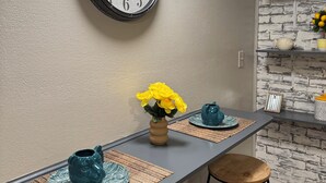 A kitchen with a wall clock, a bar stool, a bar counter, and a brick-patterned wall. - Convenient 1-BR - Fenced Backyard - Extended Stays wanted (Huntington)
