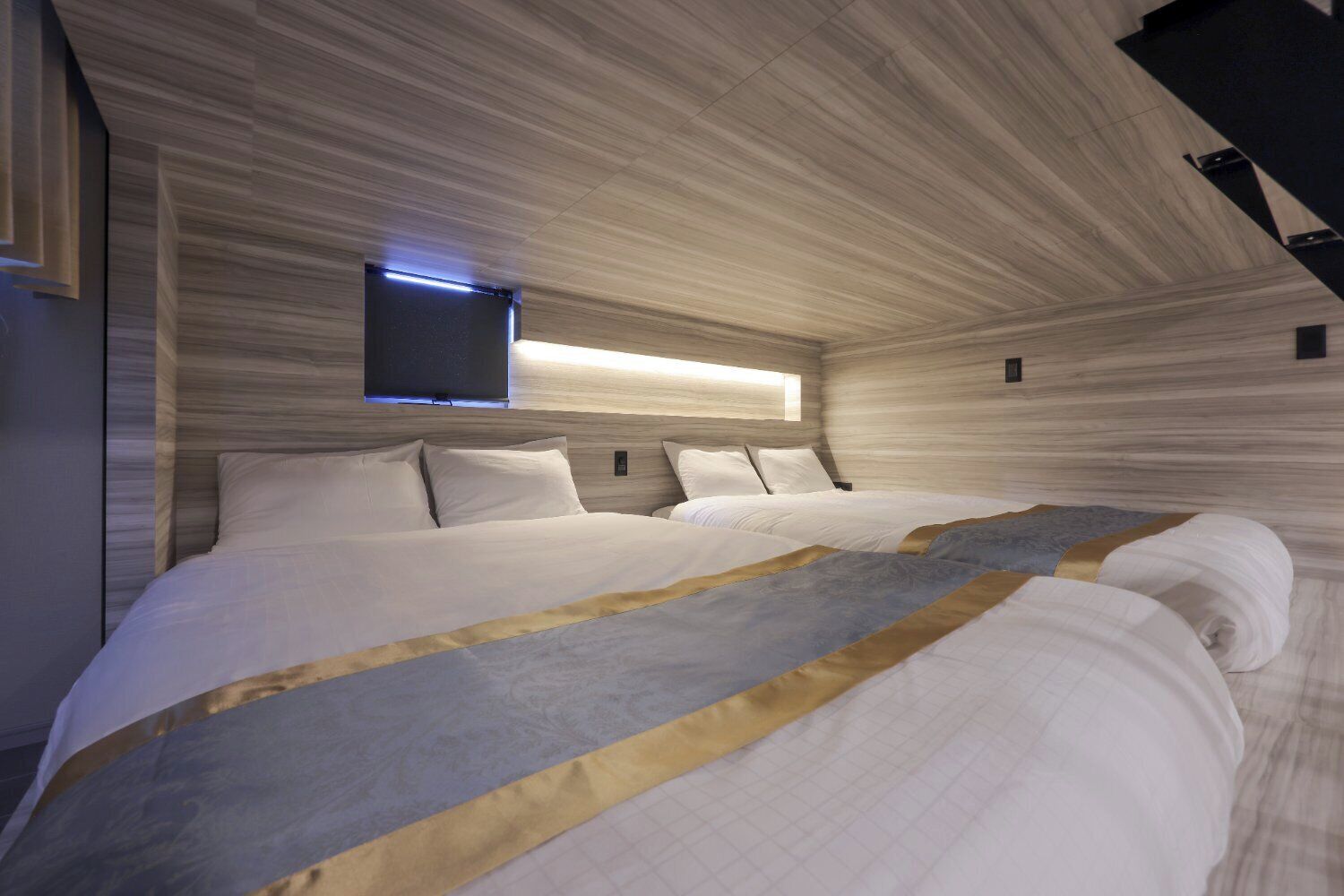 A modern bedroom with a large bed, a flat-screen TV mounted on the wall, and a unique wooden ceiling design.