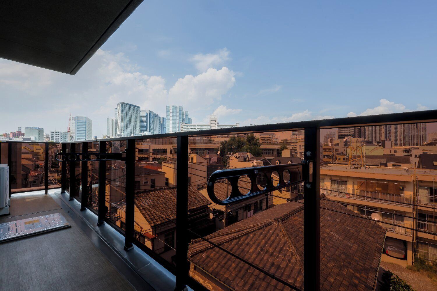 Un balcón con baranda de metal que da a una vista urbana con edificios modernos y tradicionales.