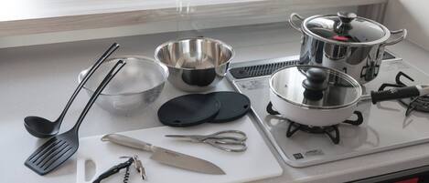 A kitchen counter with various cooking utensils and appliances, including a pot, a strainer, and a cutting board.