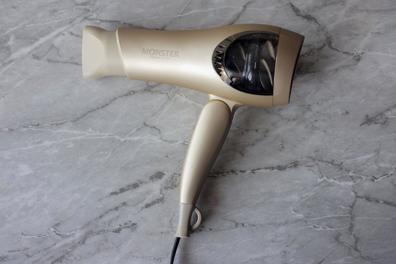 A hair dryer with a beige handle and a transparent front panel, placed on a marble surface.