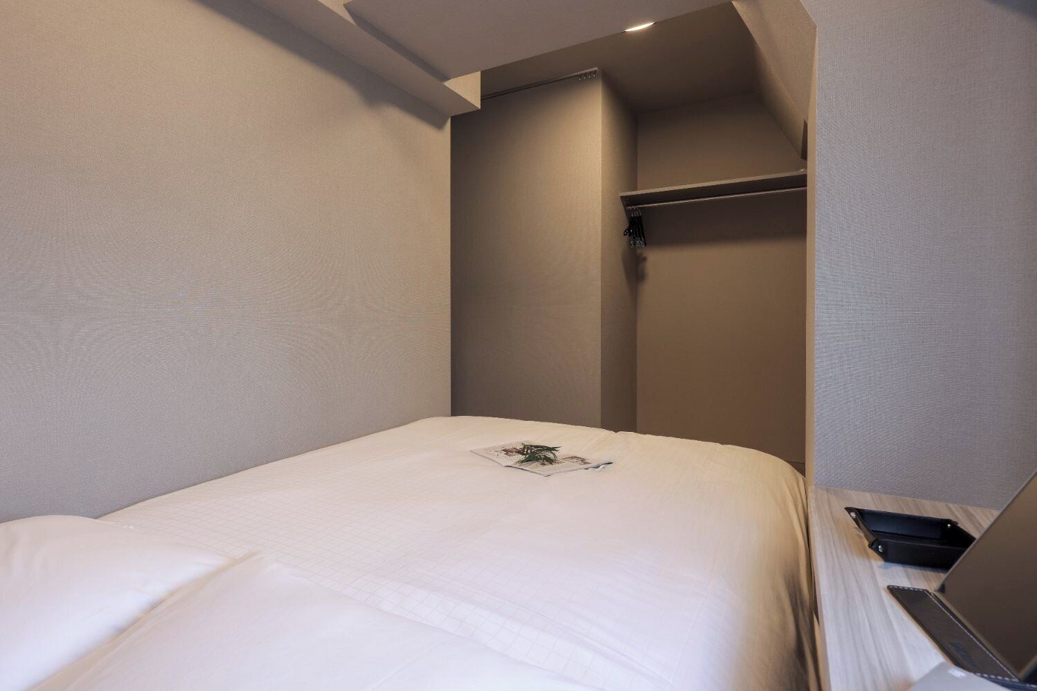 A small, neatly made room with a single bed, a desk with a laptop, and a wardrobe.