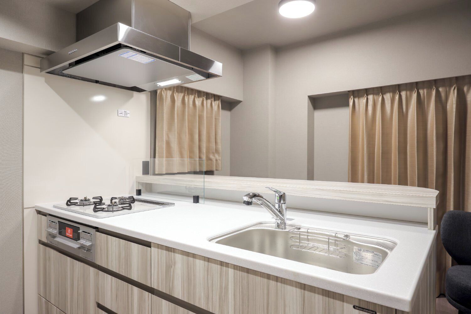 A compact kitchenette with a gas stove, a sink, and a stainless steel range hood.