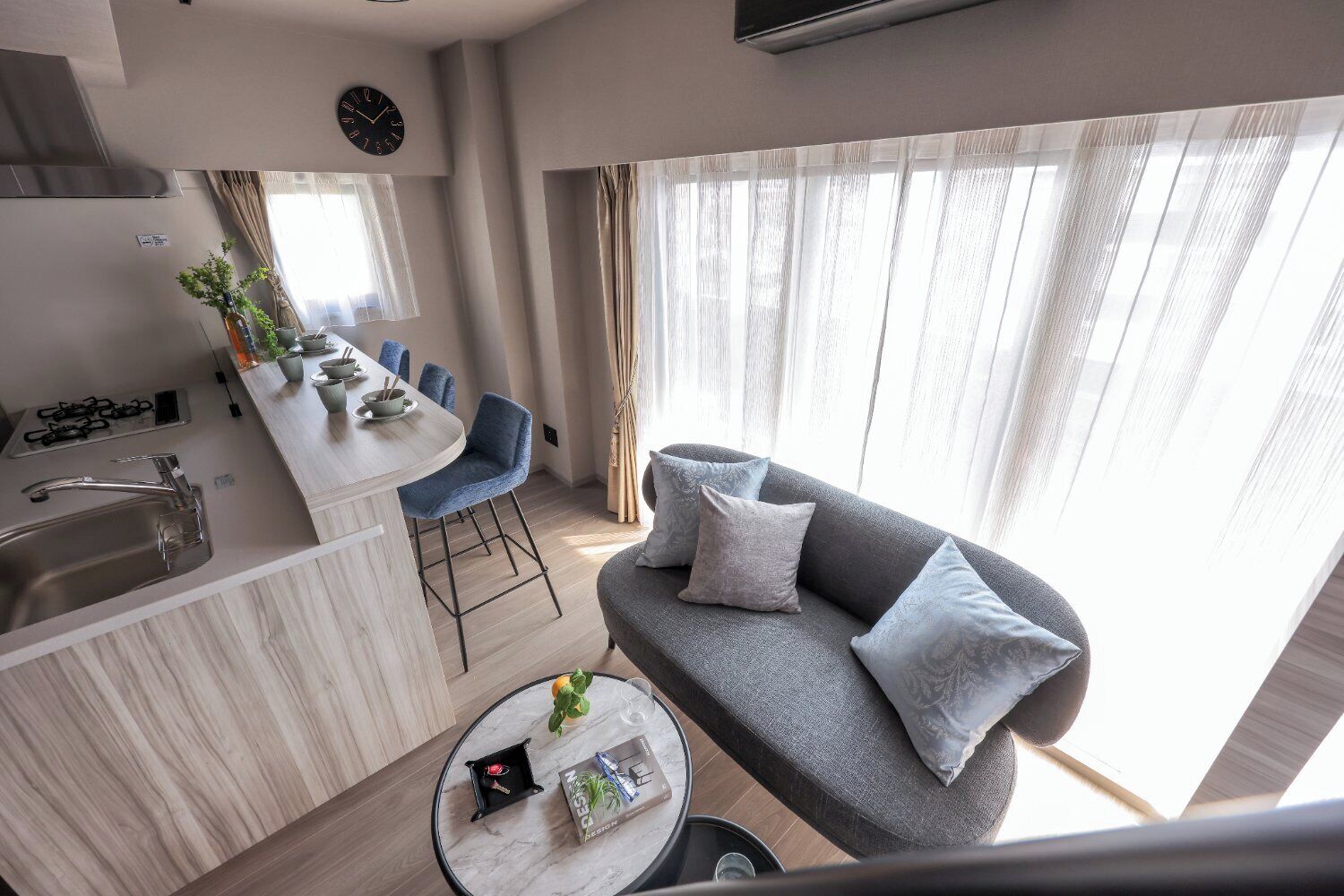 Een moderne woonkamer met een grijze bank, een salontafel en een keukenhoek met een spoelbak en fornuis.