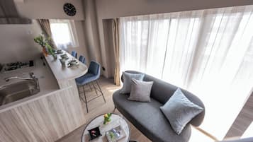 A modern living room with a grey sofa, a coffee table, and a kitchen area with a sink and stove.