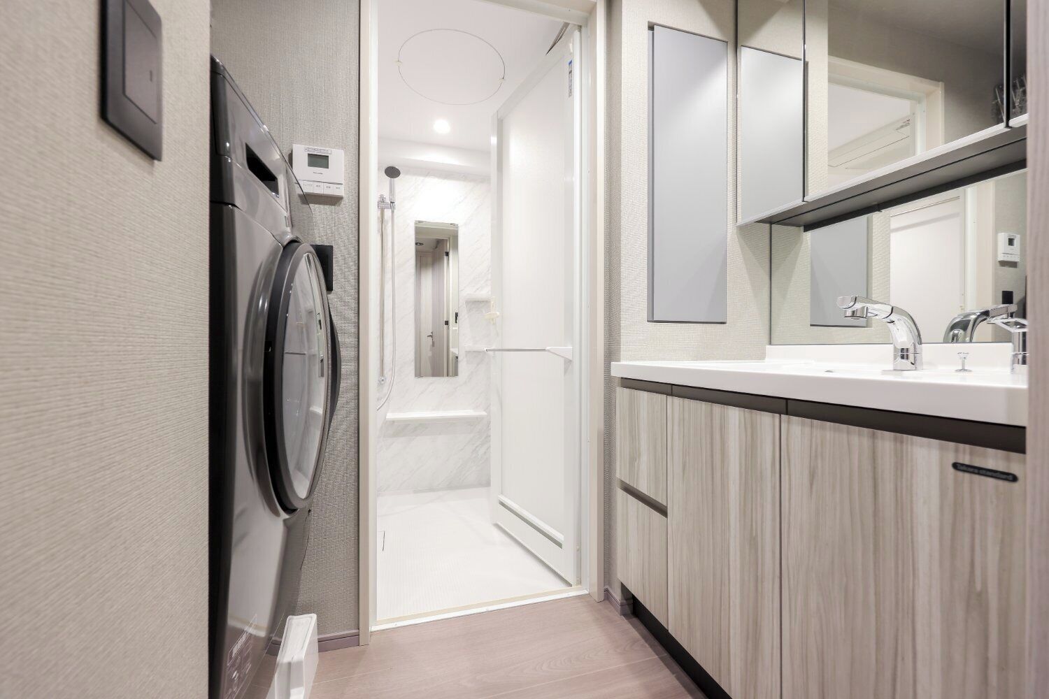A modern bathroom with a built-in washing machine, a shower, and a vanity with a mirror.
