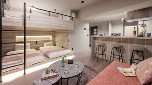 Ein modernes Hotelzimmer mit Etagenbett, einer kleinen Küchenzeile und einer Sitzecke inklusive Tisch und Stühlen.