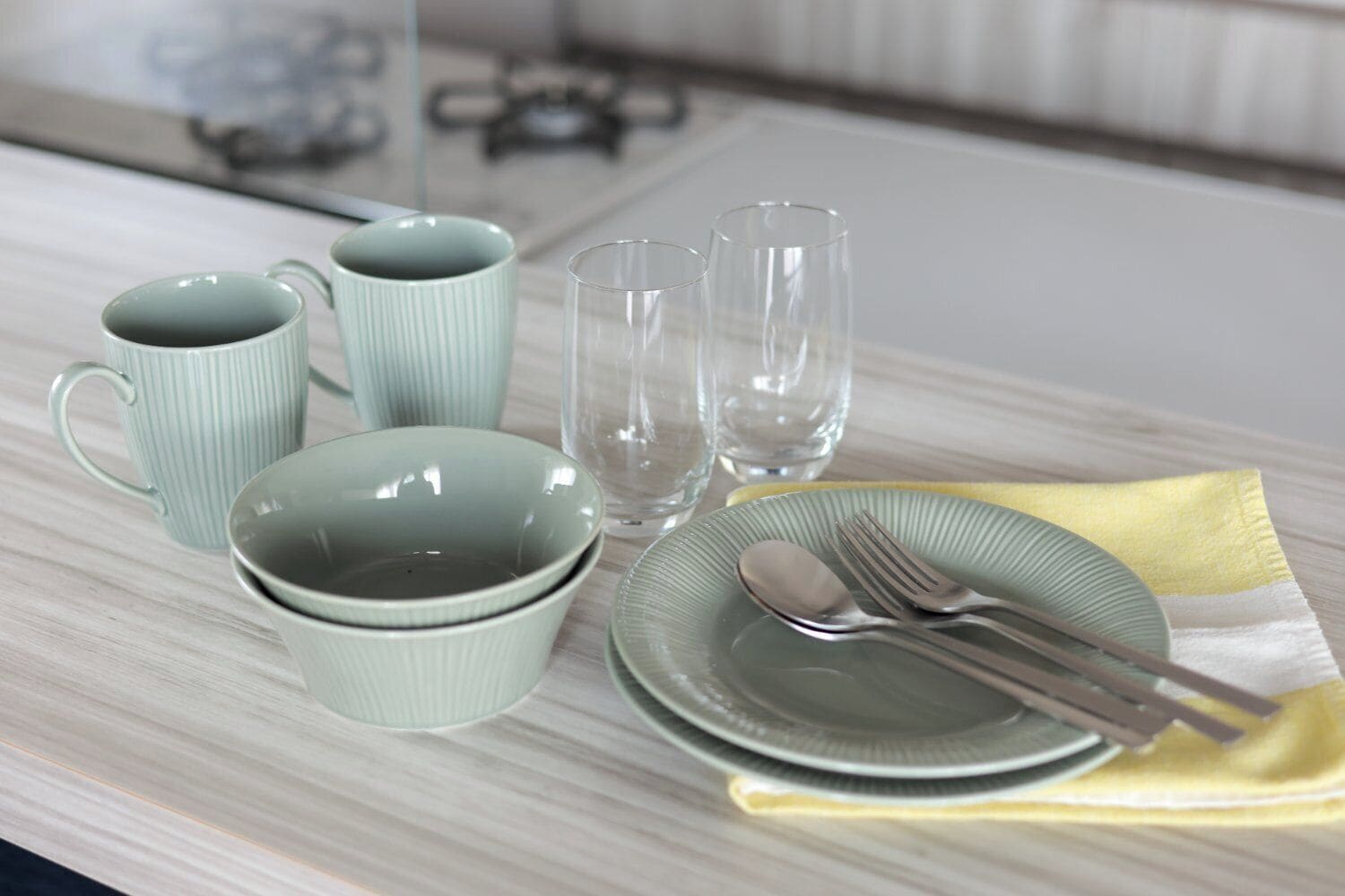A dining table with a set of green ceramic dishes, a plate with cutlery, and two clear glasses.