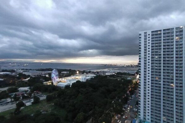 A high-rise building with a view of a park and a Ferris wheel in the distance. - Exceptional view of Manila Bay coastline (Pasay)