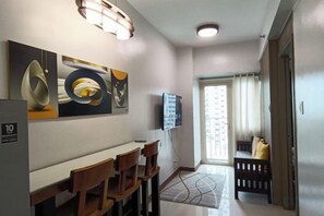 A hotel room with a dining area, a television, a window with curtains, and a door. - Exceptional view of Manila Bay coastline (Pasay)