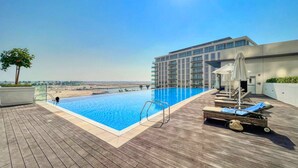 A rooftop pool with a clear view of the cityscape, surrounded by lounge chairs and a modern building. - Cove Residences - Creek Harbour Dubai (Dubai)