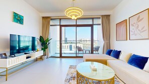 A modern living room with a flat-screen TV, a sofa, a coffee table, and a balcony with a view of buildings. - Cove Residences - Creek Harbour Dubai (Dubai)