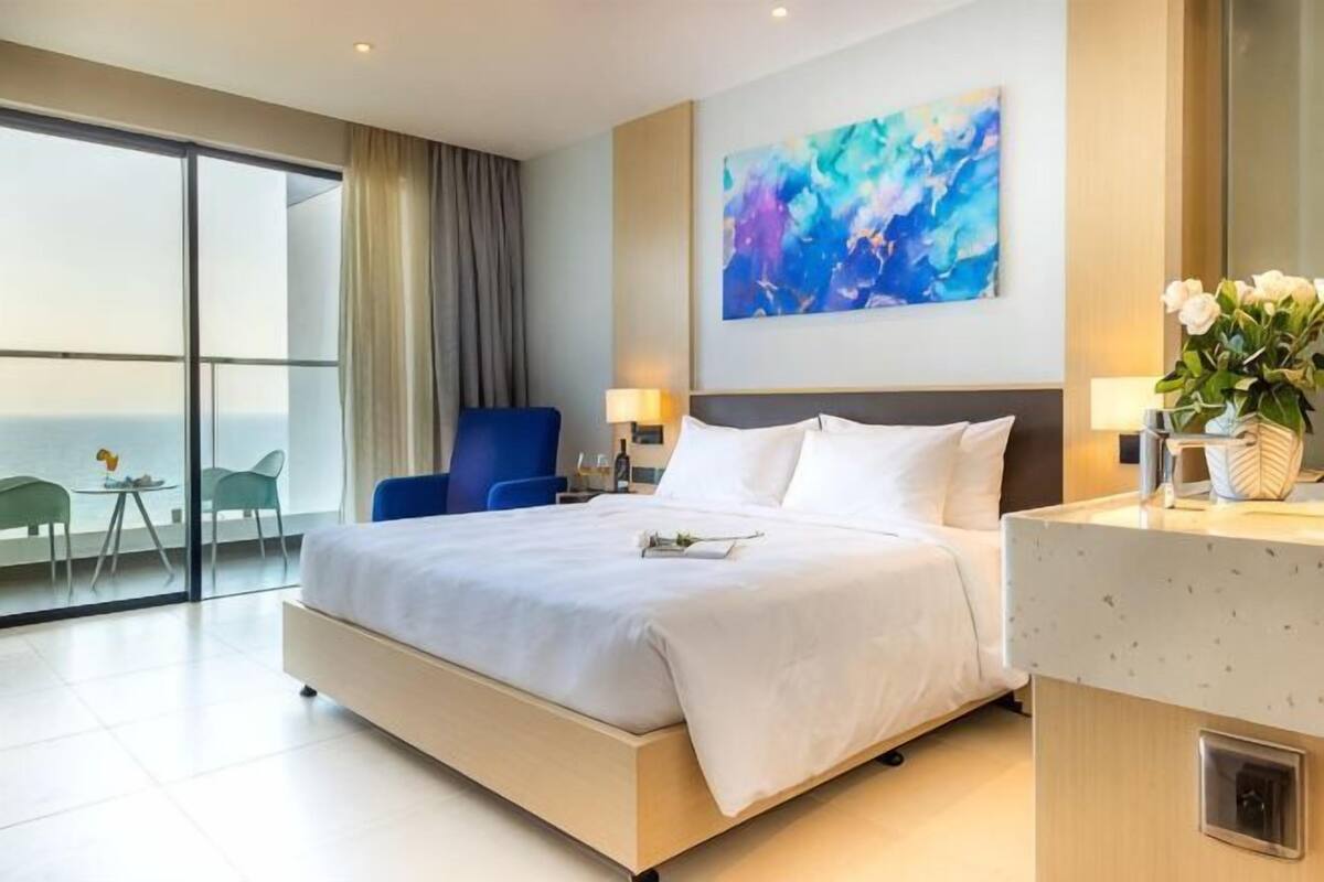 Camera d'albergo con un letto grande, una scrivania, una sedia, vista sull'oceano e un quadro appeso al muro.