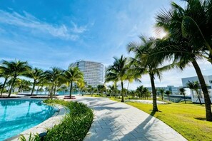 Ein Poolbereich mit blauem Himmel, Palmen und einem modernen Gebäude im Hintergrund.