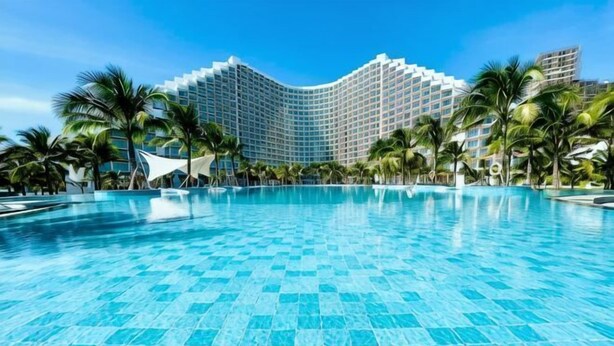A large swimming pool with a tiled surface, surrounded by palm trees and a hotel building in the background. - Sun SeaView Cam Ranh Resort (Cam Ranh)