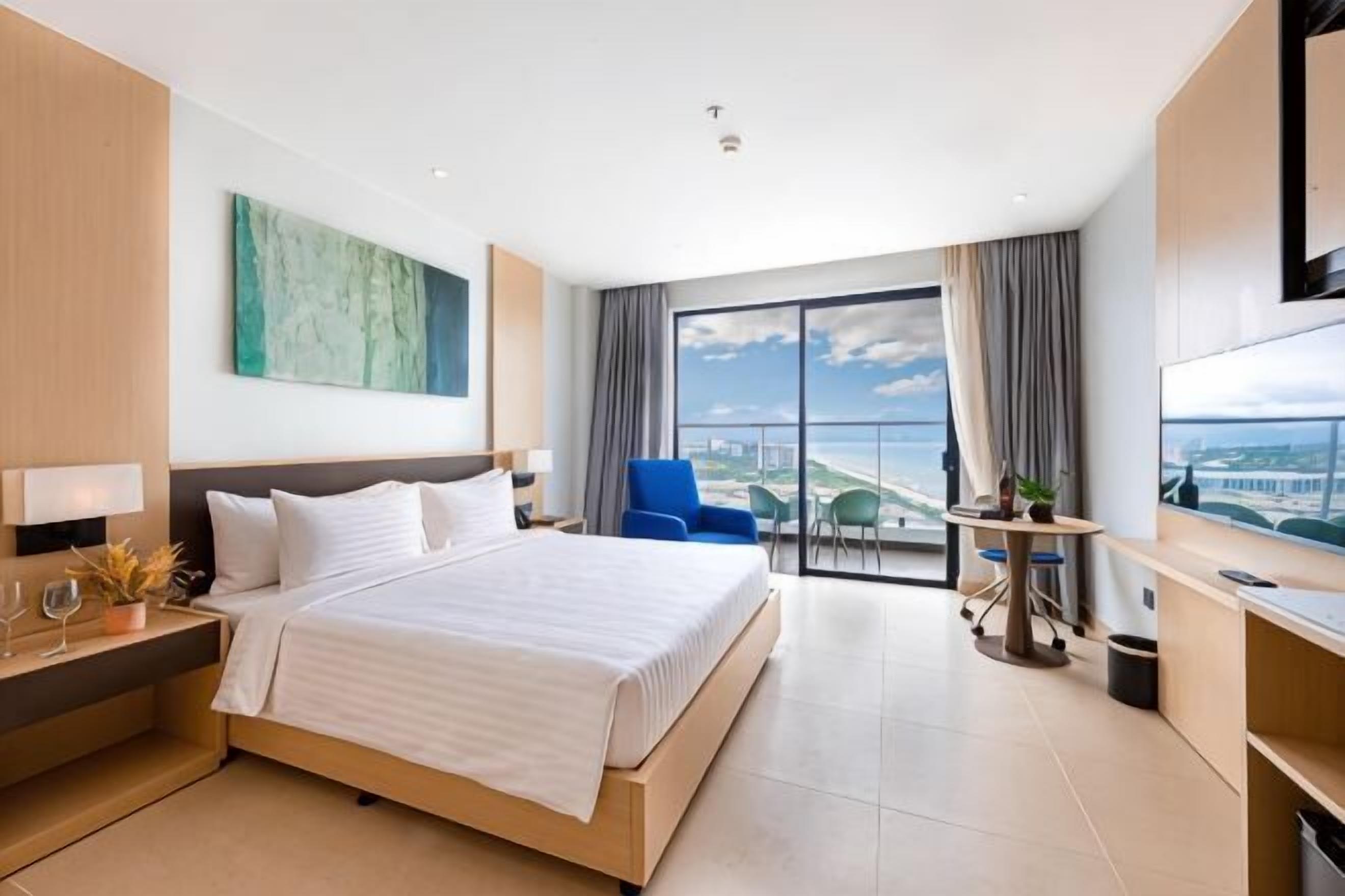 Ein Hotelzimmer mit einem großen Bett, einem Schreibtisch, einem Sessel, einem Fernseher und einem Balkon mit Aussicht.