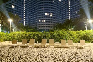 Een strand met ligbedden en een gebouw op de achtergrond.