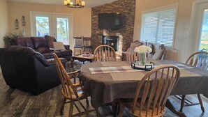 A living room with a fireplace, a dining area with a table and chairs, and a large window with blinds. - Vineyard & Valley View Cottage w/hot tub
Tranquil Farmhouse w/stunning sunsets. (Templeton)