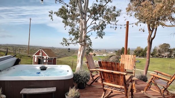 A wooden deck with a hot tub, wooden chairs, and a view of the countryside. - Vineyard & Valley View Cottage w/hot tub
Tranquil Farmhouse w/stunning sunsets. (Templeton)