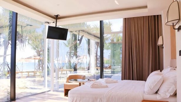 A bedroom with a large bed, a TV, and a view of the beach. - Mirror Mirror Hotel Cafe & Restaurant (Klaeng)