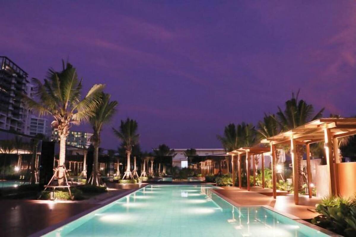 A swimming pool with palm trees and a covered area, surrounded by buildings.