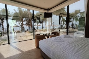 A bedroom with a large bed, a TV, and a view of the beach. - Mirror Mirror Hotel Cafe & Restaurant (Klaeng)