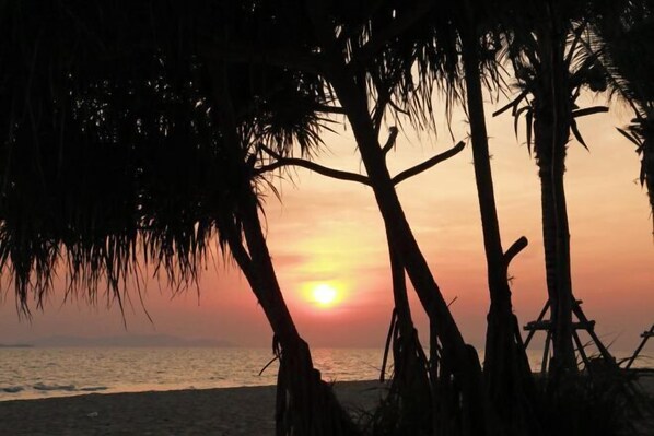 A sunset over the ocean with silhouettes of palm trees. - Mirror Mirror Hotel Cafe & Restaurant (Klaeng)