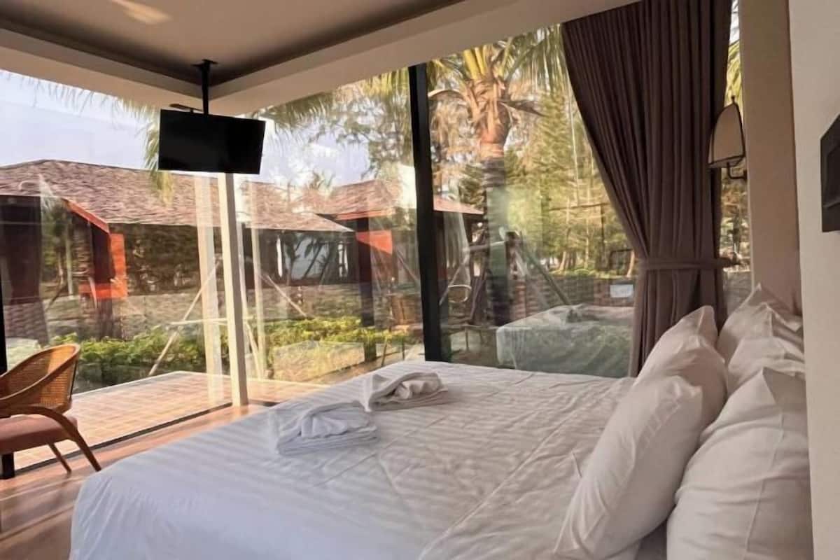A bedroom with a large bed, a TV, and a view of a garden.