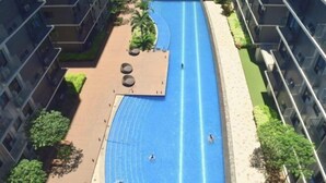 A swimming pool surrounded by modern apartment buildings, with a few people swimming. - Callie's Cozy Staycation (Pasay)