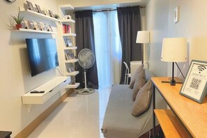 Una moderna camera d'albergo con televisore a schermo piatto, ventilatore, divano, comodino con lampada e mensola con foto incorniciate.