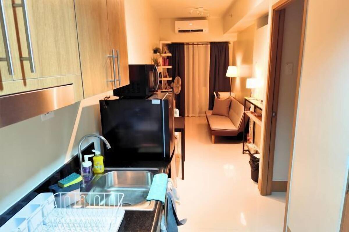A compact hotel room with a kitchenette, a sofa, and a small table.