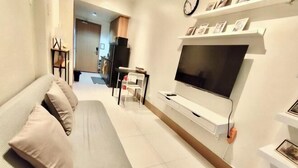 A modern living room with a sofa, a TV mounted on a wall, and a dining area in the background. - Callie's Cozy Staycation (Pasay)
