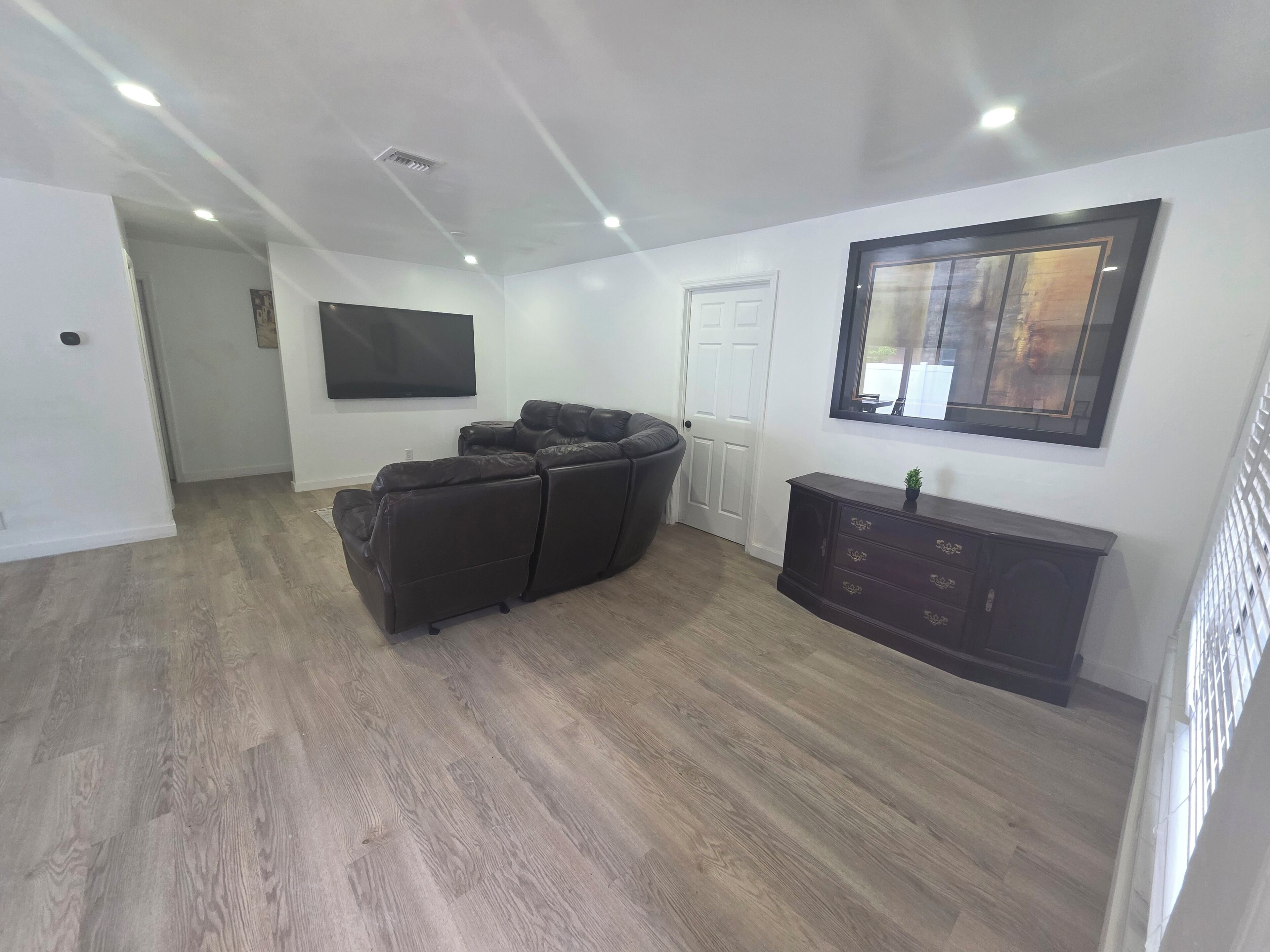 A living room with a sectional sofa, a dark wooden cabinet, and a flat-screen TV mounted on the wall.