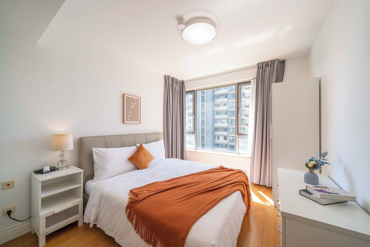 Une chambre à coucher avec un lit, une table de chevet, une lampe et une fenêtre avec des rideaux.